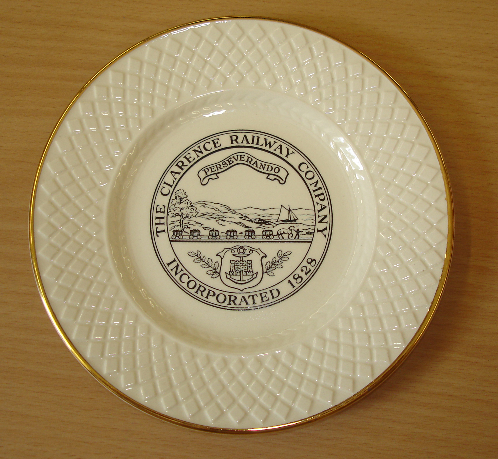 White circular plate with gold trim. Clarence Railway crest in centre.